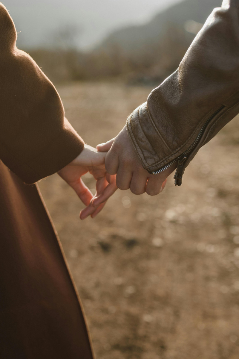 Zwei Menschen halten sich an den Händen im Freien, die Szene ist ruhig und von warmem Licht geprägt.