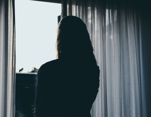 Silhouette einer Person, die durch halbgeöffnete Vorhänge nach draußen blickt und die Dämmerung beobachtet.