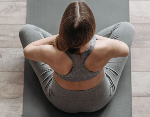 Eine Frau sitzt auf einer Yogamatte, mit den Armen vor der Brust.