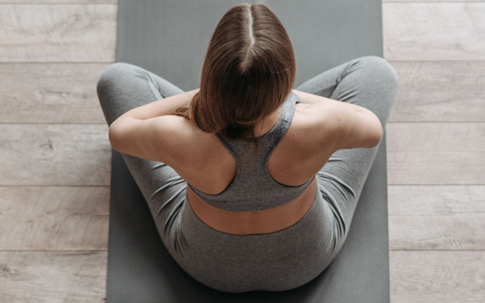 Eine Frau sitzt auf einer Yogamatte, mit den Armen vor der Brust.