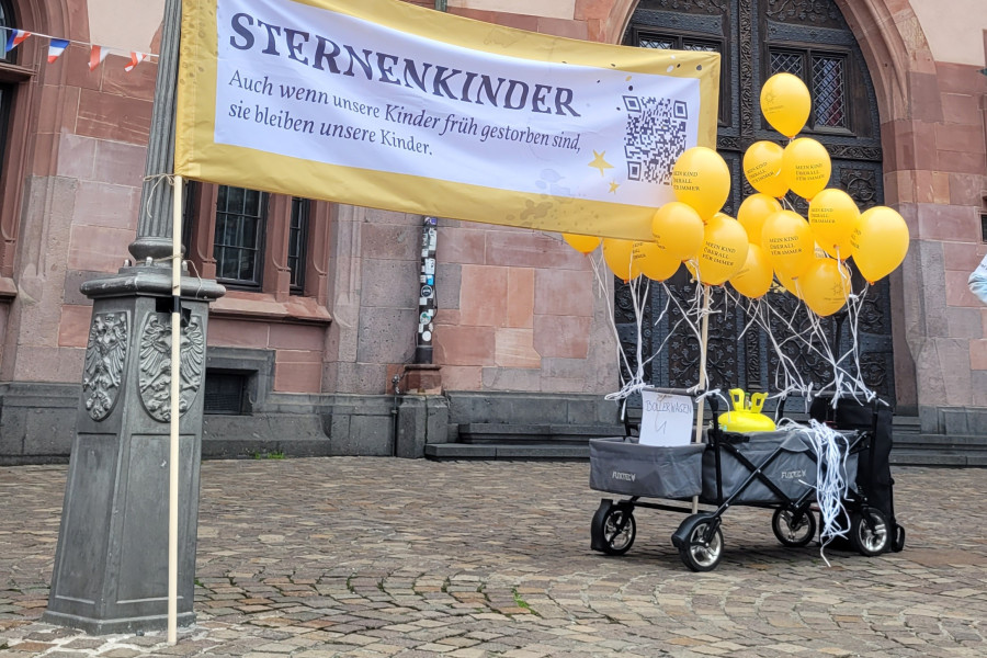 Ein Bollerwagen mit gelben Luftballons und einem Banner zum Gedenken an Sternenkinder vor dem historischen Frankfurter Rathaus