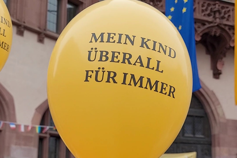 Gelber Luftballon mit dem Aufdruck 'MEIN KIND ÜBERALL FÜR IMMER', gehalten von einer Person.