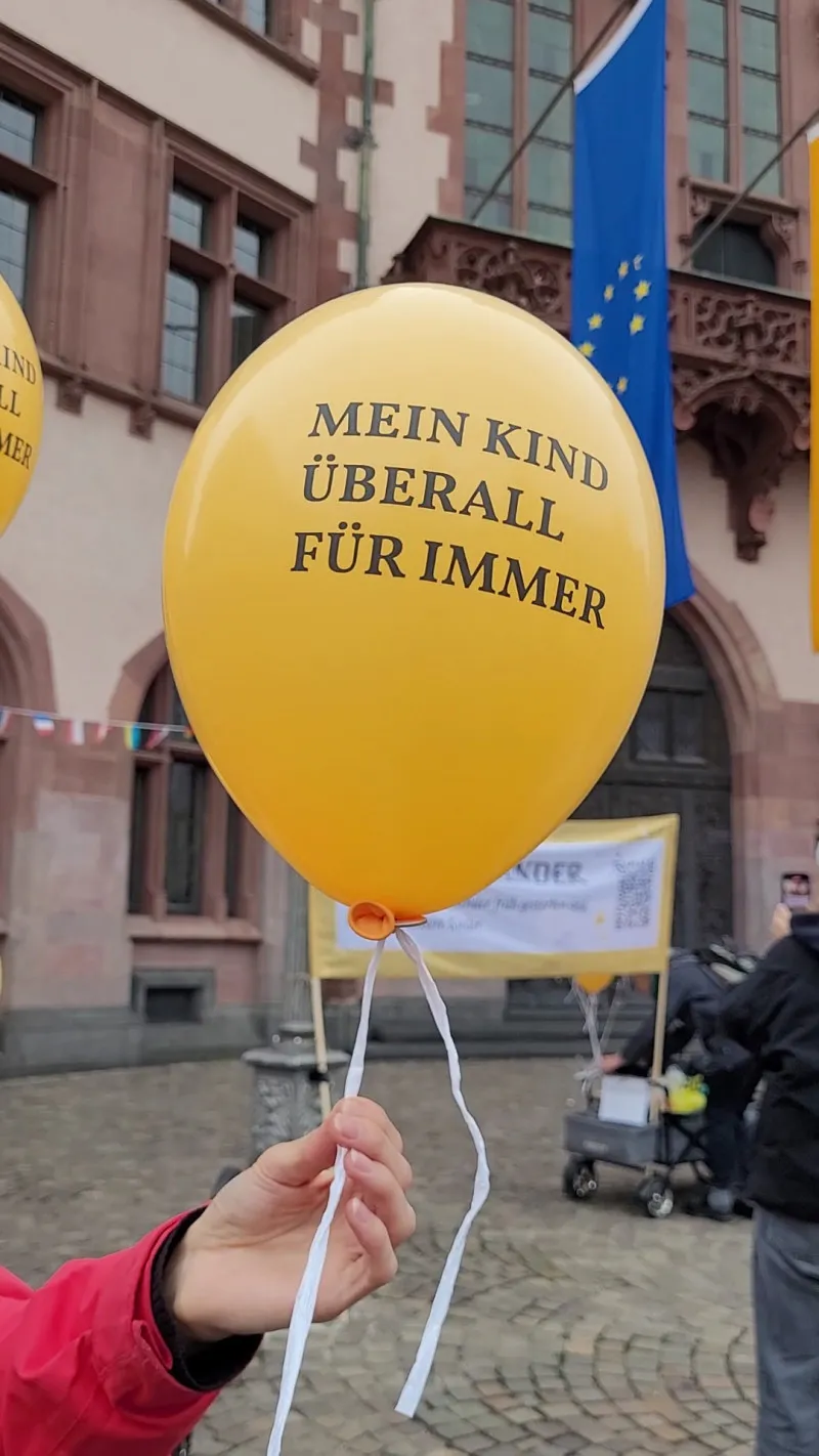 Gelber Luftballon mit dem Aufdruck 'MEIN KIND ÜBERALL FÜR IMMER', gehalten von einer Person.