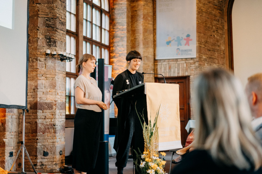 Die beiden Vorstandsvorsitzenden stehen am Rednerpult und sprechen vor dem Publikum bei einer Fachveranstaltung.