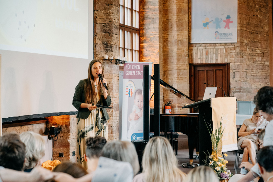 Moderatorin spricht am Mikrofon vor Fachpublikum bei einer Veranstaltung zum Thema prä- und perinataler Kindstod.